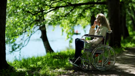 Inclinación-hacia-abajo-de-la-mujer-mayor-discapacitada-sentado-en-silla-de-ruedas-cerca-del-lago-en-el-parque-solo-y-limpiando-las-lágrimas