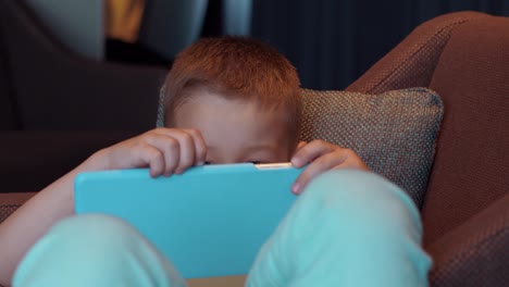 Child-lying-in-arm-chair-and-watching-cartoons-on-pad