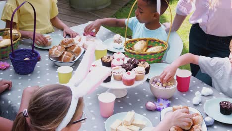 Gruppe-von-Kindern-mit-Hasenohren-sitzen-am-Tisch-draußen-genießen-Osterfeier-mit-Eltern---in-Zeitlupe-geschossen