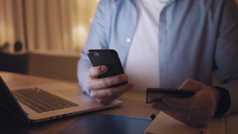 Man-typing-credit-card-data-on-smartphone-over-the-desk