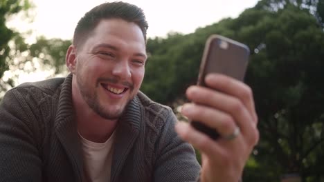 Retrato-de-joven-guapo-feliz-usando-la-aplicación-móvil-al-aire-libre