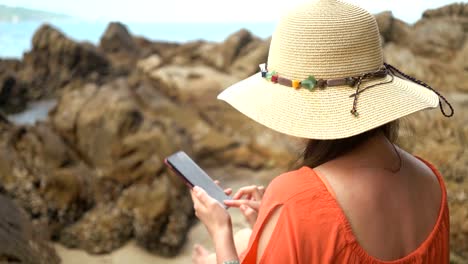 young-beautiful-woman-using-phone-for-communicate-in-social-networks-and-sitting-on-a-stone-near-sea