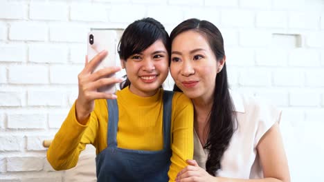 Happy-Asian-teenage-daughter-and-middle-aged-mother-taking-selfie-or-video-calling