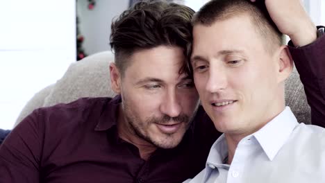 Gay-couple-relaxing-on-couch.-Head-close-together-intimate.