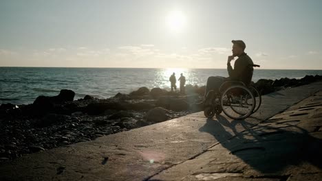 Lonely-adult-disabled-man-is-contemplating-sea-view,-sitting-on-seashore