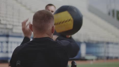 Atleta-en-silla-de-ruedas-y-entrenador-lanzando-pelota-de-medicina