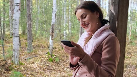 Happy-attractive-woman,-in-the-autumn-spring-forest,-communicates-on-social-networks-via-phone