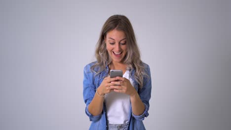 Schöne-blonde-Frau-mit-Smartphone-Posting-auf-ihrem-Blog-in-sozialen-Medien-und-glücklich-mit-Likes-von-Anhängern-und-Online-Geschäft.-Isoliert-auf-neutralem-Hintergrund.-Im-Unternehmer-,-Online-Netzwerk--und-Technologiekonzept.