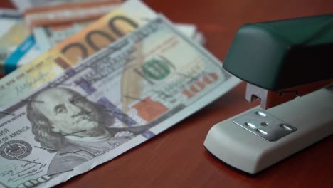 The-stapler-fastens-the-dollar-and-euro-notes-with-iron-clips.-Stapler-with-paper-clips-on-the-background-of-banknotes.-Counterfeit-money