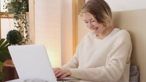 Woman-laughing-while-using-laptop-in-bed