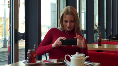 Una-joven-atractiva-mujer-se-sienta-en-una-mesa-en-un-café-y-toma-una-foto-de-su-comida