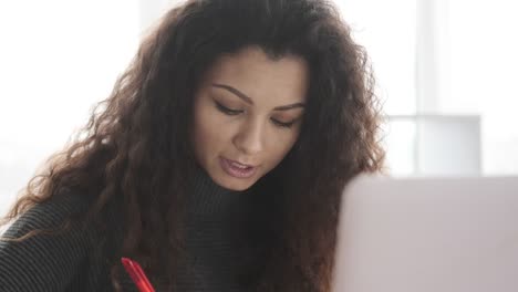 Businesswoman-writing-notes-while-video-chatting-at-office