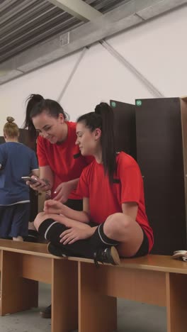 Zwei-Fußball-Mädchen-mit-Smartphone-in-Locker-Room