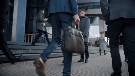 Close-Up-Leg-Shot-of-a-Businessman-in-a-Suit-Commuting-to-the-Office-on-Foot.-He's-Carrying-a-Leather-Case.-Other-Managers-and-Business-People-Walk-Nearby.-Cloudy-Day-on-a-Downtown-Street.