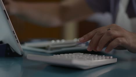 Close-up-hand-of-woman-checking-account-balance-and-calculating-expenses-in-the-living-room-at-home.-Housewife-working-with-calculator-and-digital-tablet-on-the-desk-during-quarantine-with-COVID-19-pandemic-situation.