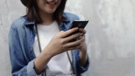 Smiling-of-asian-woman-wearing-retro-fedora-hat-using-smartphone-typing-message,-browsing-social-media-sharing-trip-with-her-friends-on-holiday-summer.