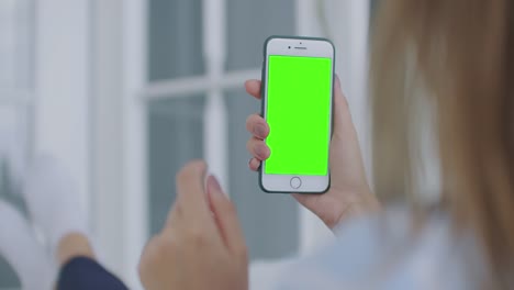 Woman-using-for-video-call-mobile-phone-vertical-green-screen.-Female-holding-in-hand-portable-gadget-close-up-indoors-home-living-room.-Mock-up-for-tracking-or-watching-content.