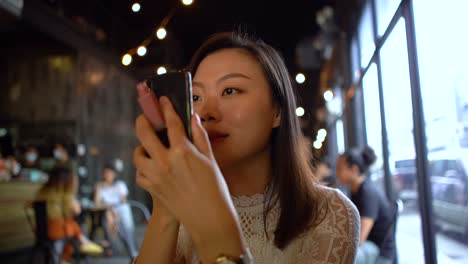 Joven-mujer-asiática-aplicando-lápiz-labial-usando-teléfono-inteligente