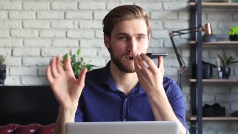 Confident-business-man-holding-smartphone-near-mouth-for-recording-voice-message-or-activating-digital-assistant.