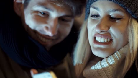 Young-couple-watching-photos-on-smartphone-at-night-in-a-city-street.