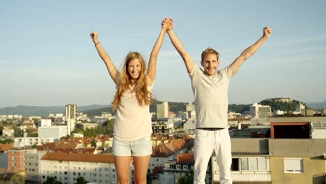 CLOSE-UP:-Happy-Bruder-und-Schwester-stehen-auf-Dach,-die-Hände-in-den-Himmel