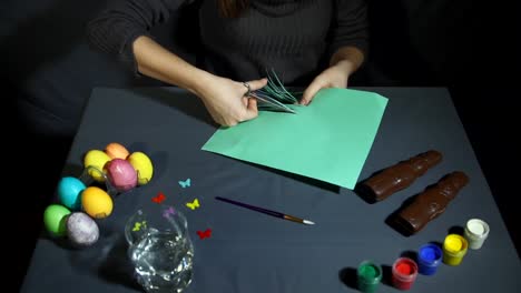 Female-hands-cut-into-thin-fringe-the-green-paper-with-scissors-over-gray-table.