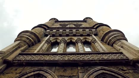 tilt-up-panorama-of-facade-of-tower-of-medieval-stronghold,-stained-glass-windows,-bas-reliefs