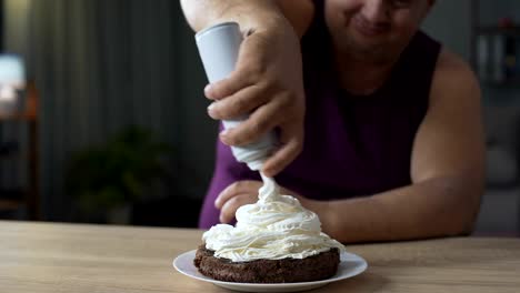 Fat-male-decorating-cake-with-whipped-cream-and-putting-cherry-on-the-top