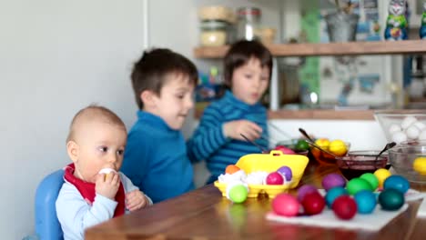 Three-children,-brothers,-coloring-and-painting-easter-eggs-at-home-in-kitchen-for-the-holiday