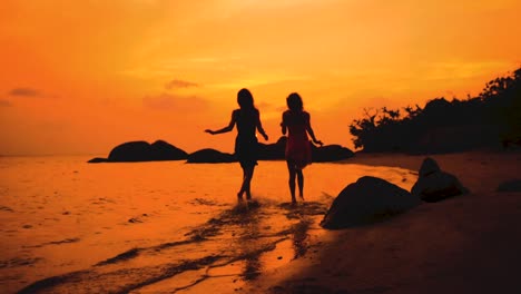 two-happy-girls-running-into-water-at-sunset-in-slow-motion