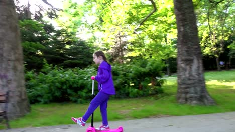 Little-child-learning-to-ride-a-scooter-in-a-city-park