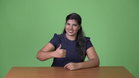 Young-overweight-beautiful-Indian-businesswoman-against-green-background