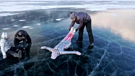 Family-is-having-fun-on-beautiful-ice-in-cracks.-Father-mother-son-and-daughter-funny-fight-on-ice,-make-sandwich-and-rest.-Man,-woman-and-children-are-resting-on-lake-of-Baikal.