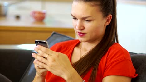 A-beautiful-girl-in-a-red-dress-writes-a-message-in-her-mobile.-Then-he-looks-at-the-frame-and-smiles-broadly.-Social-networks