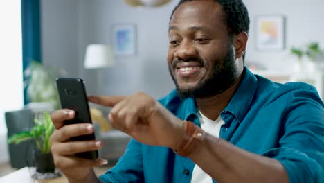 Portrait-of-the-Handsome-Young-Man-Using-Smartphone,-Browsing-in-Internet,-Checking-Social-Networks,-Scrolling-Newsfeed-while-Sitting-At-Home.