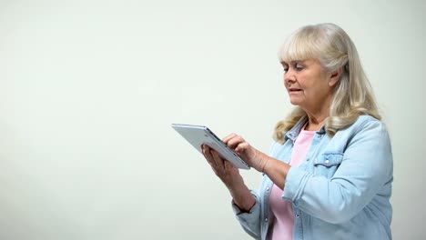 Thoughtful-elderly-lady-scrolling-screen-on-tablet,-online-banking-application