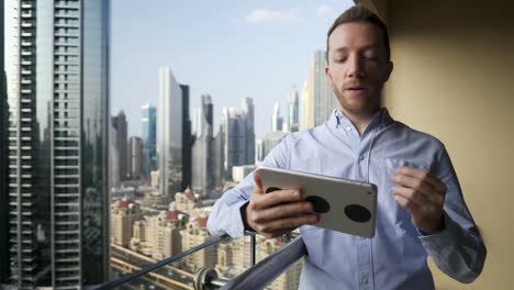 Hombre-joven-usando-la-tableta-para-hablar-y-comunicarse-con-el-fondo-de-la-vista-rascacielos