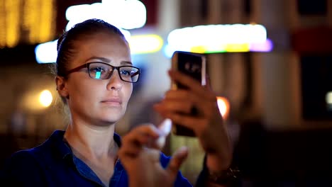 Porträt-der-jungen-schönen-kaukasischen-Frau-mit-Smart-Phone-Hand-halten-im-Freien-in-der-Stadtnacht,-lächelnd,-Gesicht-beleuchteten-Bildschirmlicht-soziales-Netzwerk,-Technologie,-Kommunikation-Konzept