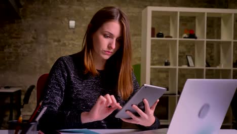 Attractive-caucasian-ginger-woman-chatting-using-tablet-and-smiling-in-the-office-background