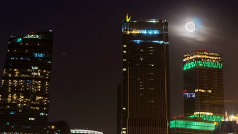 La-luna-se-eleva-sobre-la-carretera-iluminada-y-la-ciudad-nocturna,-lapso-de-tiempo