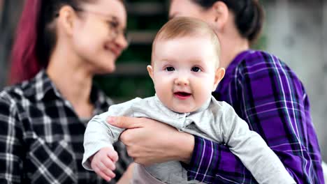 Porträt-des-süßen-kleinen-Babys-posiert-mit-Blick-auf-Kamera-weibliches-Paar-im-Hintergrund