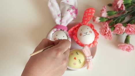 Close-up-of-female-hand-with-brush-draws-chicken-Easter-eggs-decorated-for-Easter-hares-and-chickens