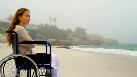 Side-view-of-young-Caucasian-woman-sitting-on-wheelchair-at-beach-4k