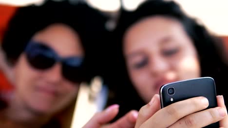 Adolescentes-sonrisa-vista-previa-de-las-redes-sociales-mensajes-en-el-teléfono-inteligente-acostado-en-la-cama-de-playa,-enfoque-selectivo