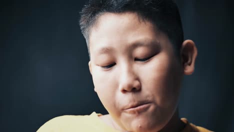 large-build-Asian-preteen-boy-eating-donut-while-touching-his-tummy,-slow-motion-in-low-light.