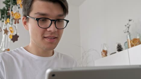 Attractive-man-at-home-using-tablet-in-kitchen-sending-message-on-social-media-smiling-enjoying-modern-lifestyle-wearing-white-shirt