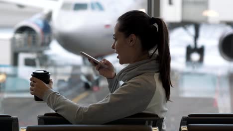 Chica-con-café-para-llevar-en-su-mano-registra-el-mensaje-de-voz-en-el-teléfono-en-el-aeropuerto