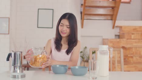 Asian-Lesbian-couple-has-breakfast-drink-juice,-corn-flakes-cereal-and-milk-in-bowl-on-table-in-kitchen-in-the-morning.