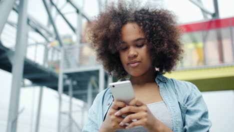 Happy-African-American-girl-looking-at-smartphone-screen-smiling-outdoors