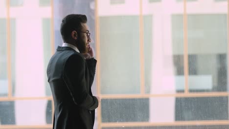 Confident-arabic-businessman-wear-suit-talking-on-phone-in-office